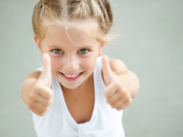 Child smiling at camera with two thumbs up