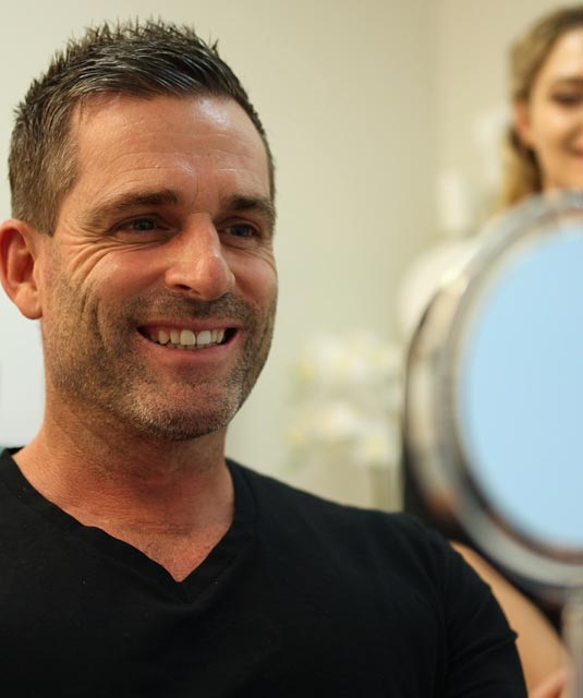 Smiling man looking at his teeth in the mirror at Bayview Dental